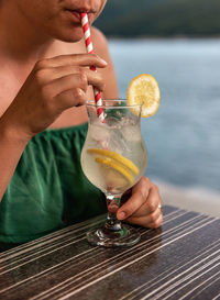 Close-up photo of woman drinking refreshing lemonade on straw in a bar by sea