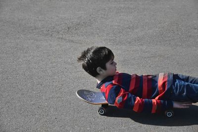 Boy lying on skateboard at street during sunny day
