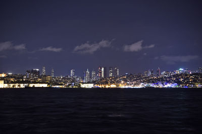 Illuminated cityscape by sea against sky at night
