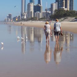 Full length rear view of senior man and woman walking at beach in city