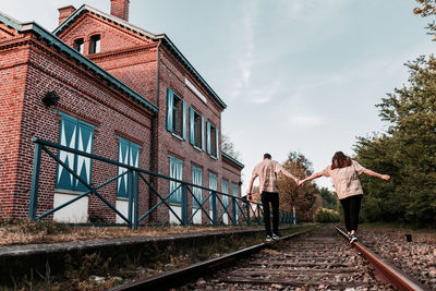 Rear view of woman walking on railroad tracks by buildings against sky