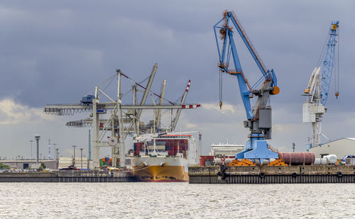 Cranes at commercial dock against sky