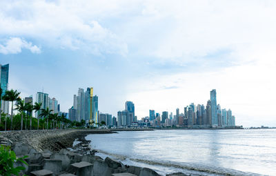 Sea by modern buildings against sky in city