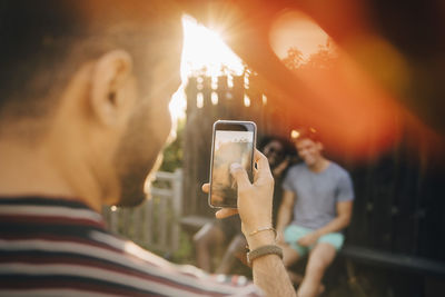 Cropped image of man photographing friends on smart phone at yard