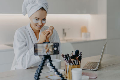 Smiling woman applying eye patches while vlogging at home