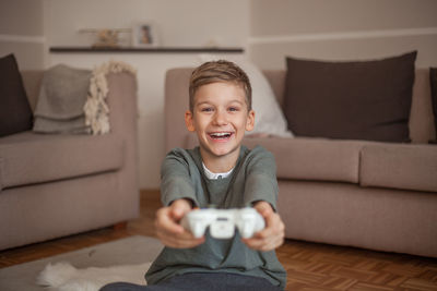 Portrait of smiling boy holding video game remote control in living room at home 