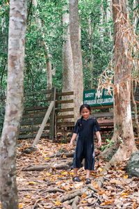 Full length of girl standing on land against tree trunk in forest