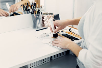 Unrecognizable female makeup artist standing at table in modern beauty studio and applying powder with brush