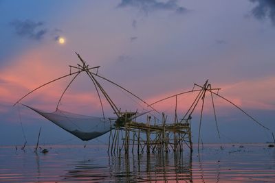 Fishing net in sea against sky at sunset