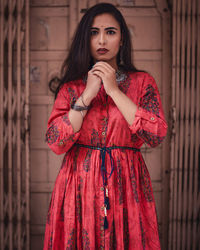 Portrait of beautiful young woman standing against red wall