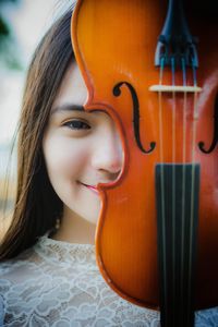 Close-up portrait of smiling young woman holding against face violin