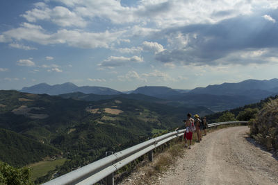 Hikers photographing mountains against cloudy sky