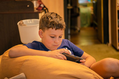 Teen caucasian boy sitting on sofa and playing on his smartphone at home