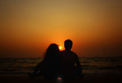 Silhouette couple on beach against orange sky