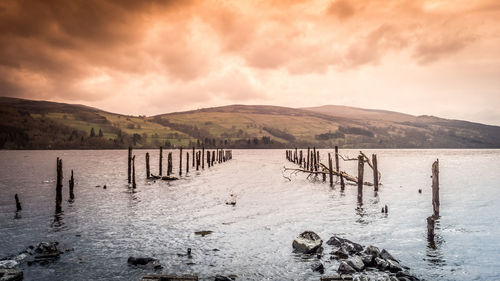 Wooden posts in lake against sky