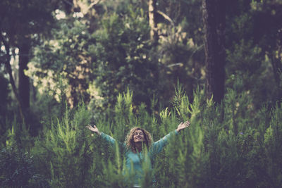 Woman with arms outstretched standing in forest