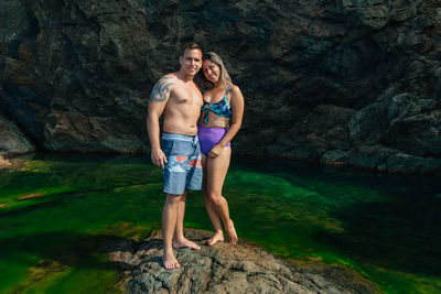 Portrait of young couple standing on rock by sea