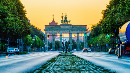 Road by illuminated city against sky during sunset