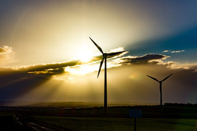 Wind turbines on field against sky during sunset