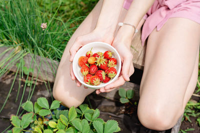A teenage girl with a bowl of strawberries in her hands sits on a bed in the garden