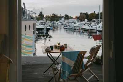 Empty chairs and tables on porch against marina at sunset