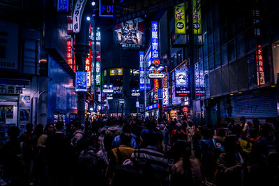 People amidst buildings with illuminated billboards in city at night