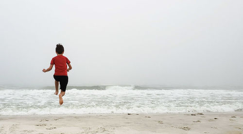 Rear view of boy jumping at beach against sky