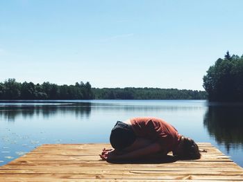 Woman relaxing by lake against sky