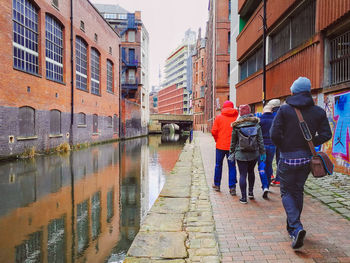 Rear view of people walking on canal in city
