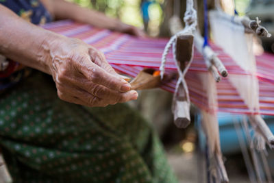 Midsection of woman weaving thread in loom