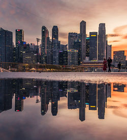 Reflection of buildings in city against sky during sunset