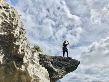 Low angle view of man standing on rock against sky