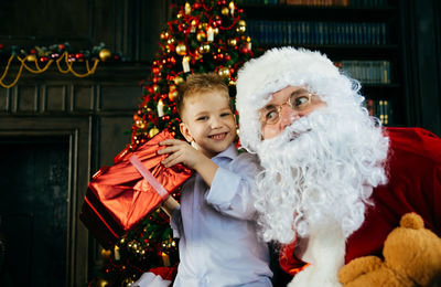 Smiling boy with santa clause against christmas tree at home