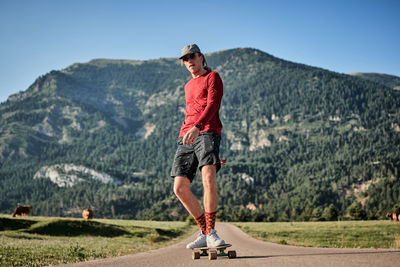 Concentrated male hipster in fancy clothes and with cap riding skateboard along road in park in summer