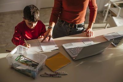 Mother assisting son in studies at dining table at home