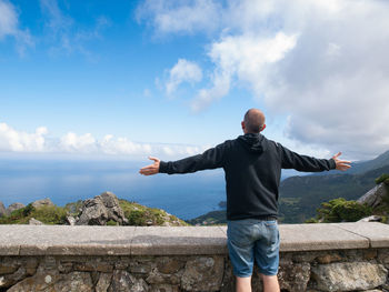 Rear view of man with arms outstretched standing by sea at observation point