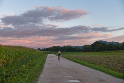 Full length of woman jogging on road amidst field at sunrise