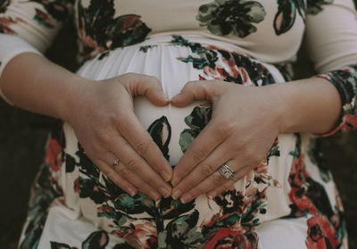 Midsection of pregnant woman making heart shape on her belly with hands