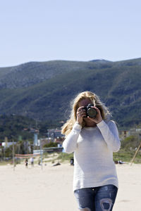 Woman photographing at beach against mountain