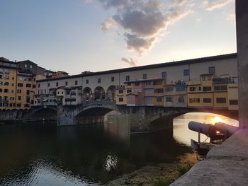 Arch bridge over river in town against sky at sunset