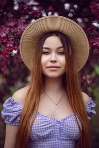 Portrait young beautiful girl teenager in a purple dress and in hat stands blooming pink apple tree