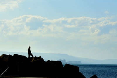 Silhouette man standing on rock by sea against sky