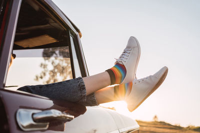 Side view of crop female chilling in vintage car with legs sticking out of window in evening in nature