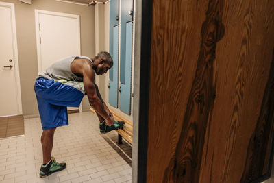 Side view of male athlete tying shoe lace in locker room