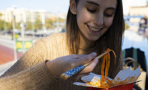 Young and beautiful girl eating some chinese noodles with chopsticks.