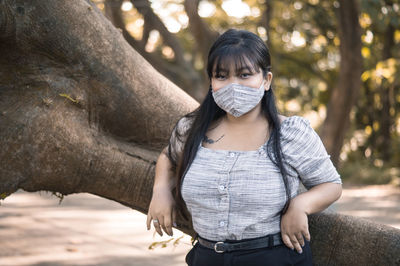 Portrait of young woman standing against tree