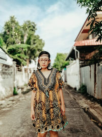 Portrait of young woman standing on footpath