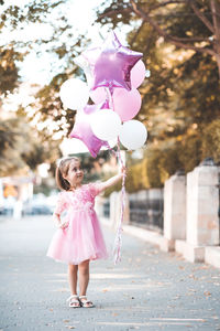 Cute girl with balloons walking on footpath