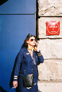 Young man using mobile phone while standing against wall