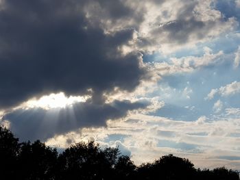 Low angle view of sunlight streaming through clouds